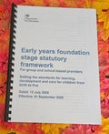 A spiral-bound booklet titled 'Early years foundation stage statutory framework' from the Department for Education, photographed flat on a background of colorful autumn leaves.